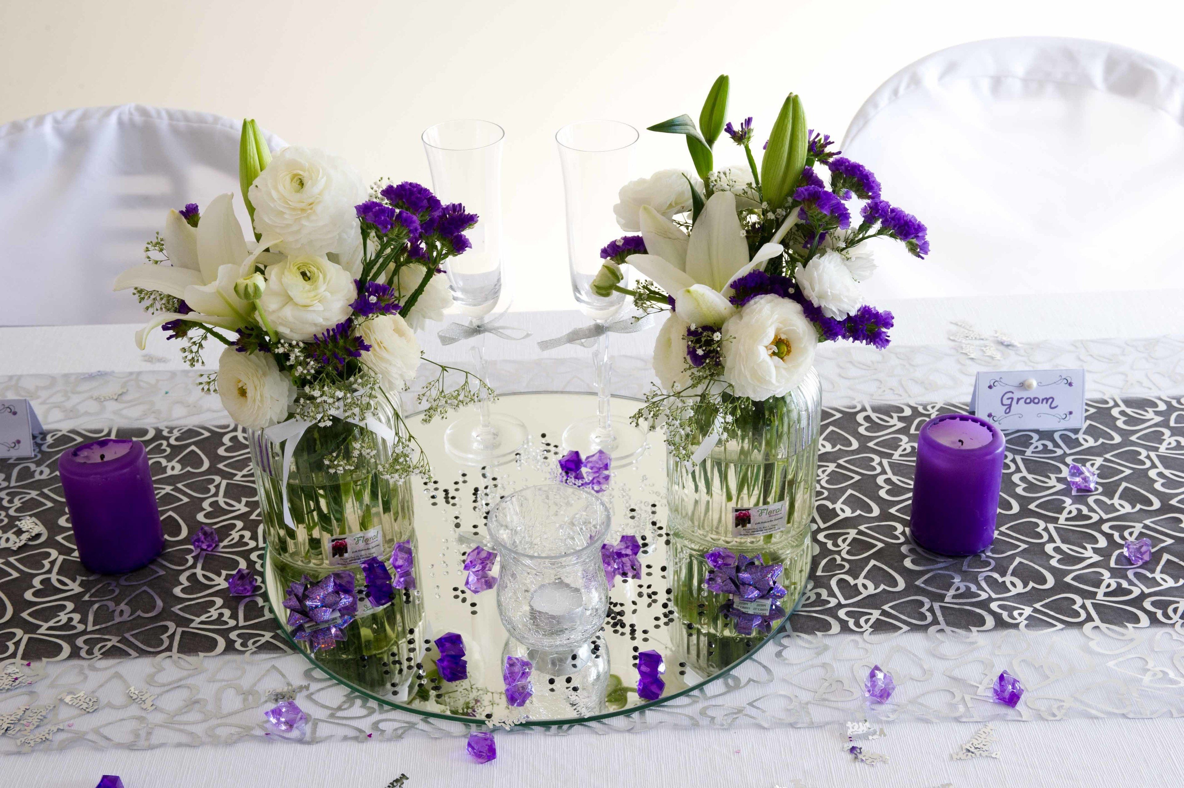 A table with a glass centerpiece containing flowers and candles, surrounded by two glass candle holders.
