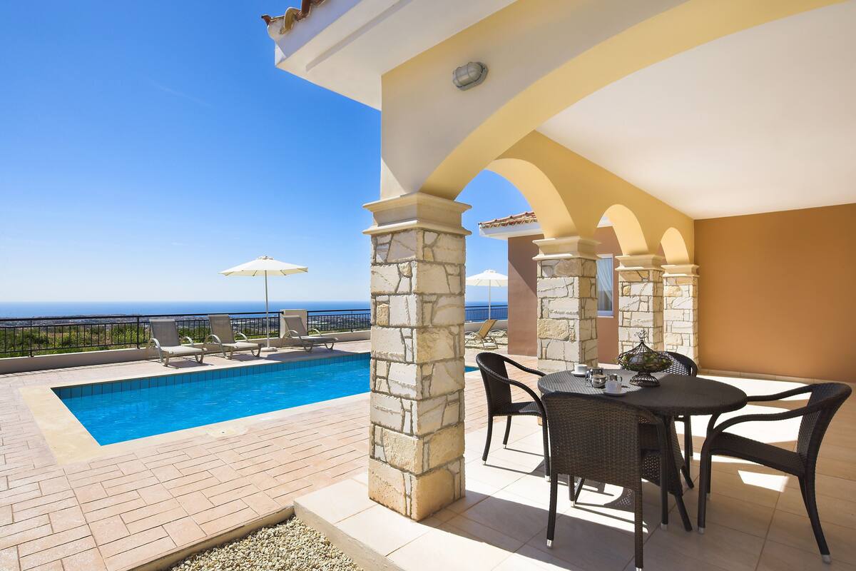 A poolside area with a view of the sea, stone pillars, and outdoor furniture.