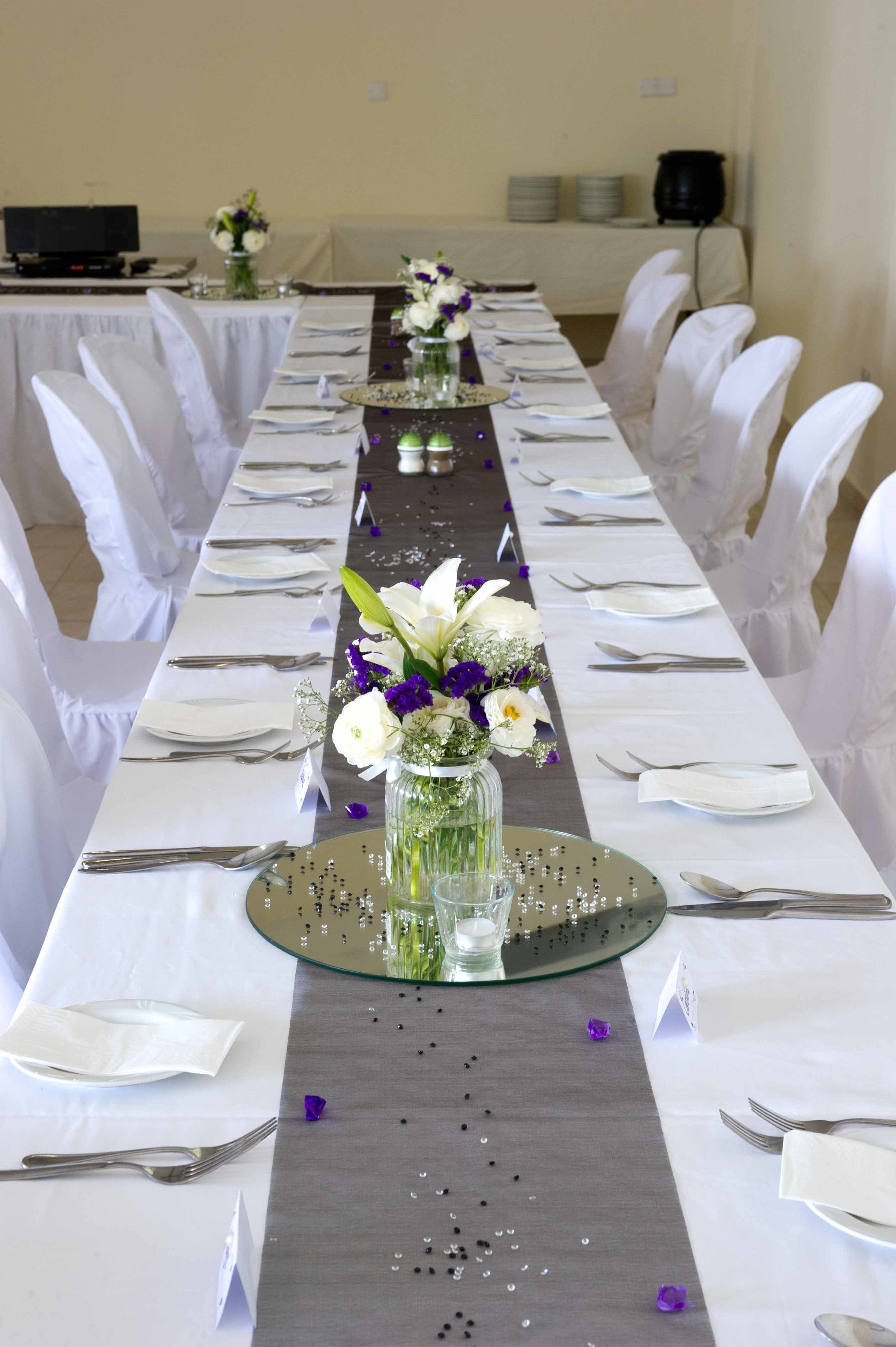 A long dining table set with white tablecloths, silverware, and a centerpiece with flowers.