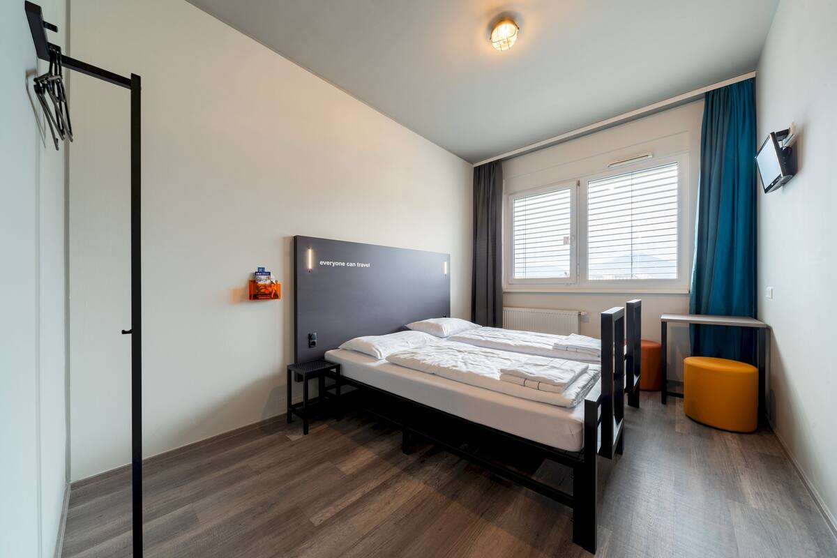 A modern hotel room with a bed, a desk, and a TV.
