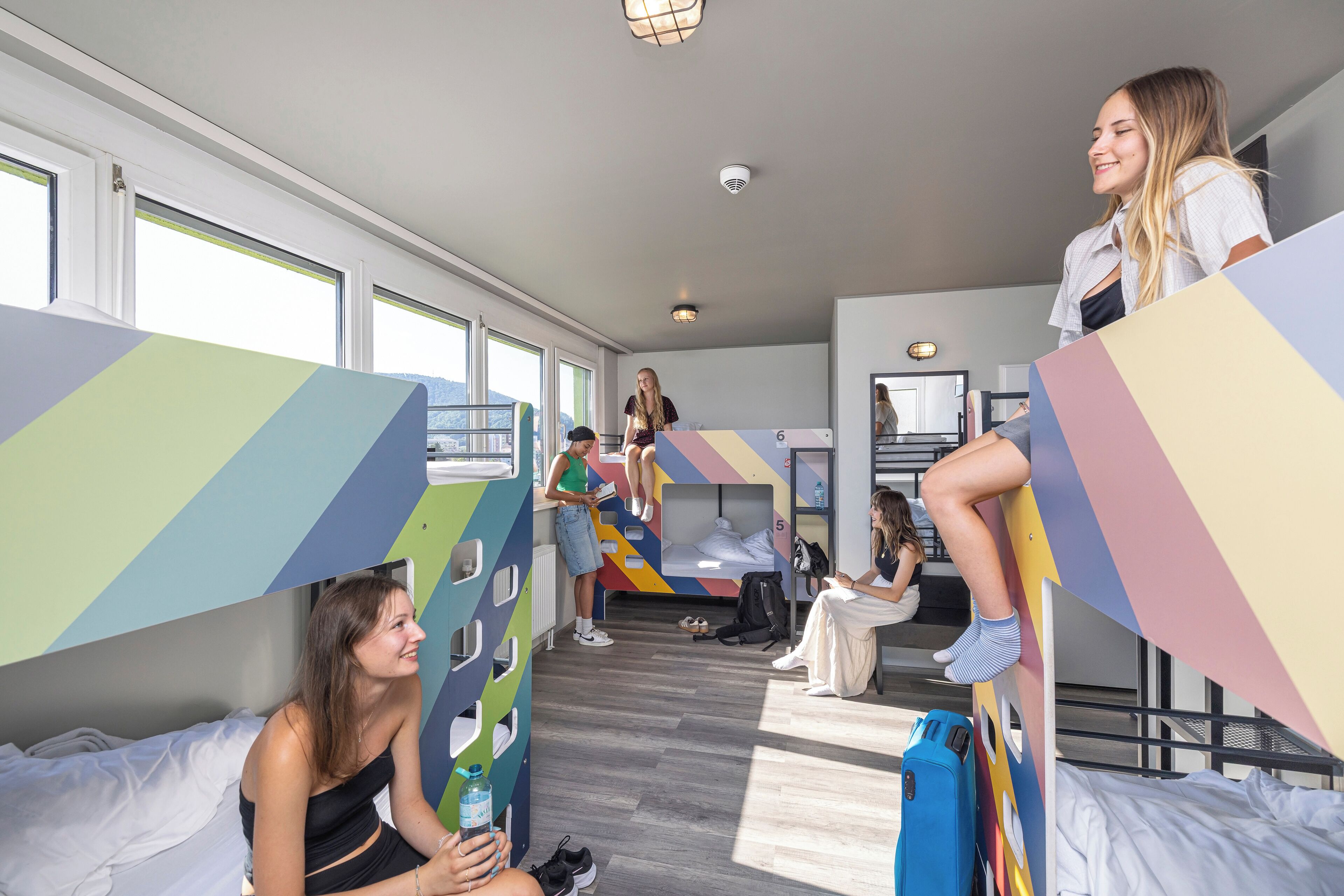 A dormitory room with bunk beds, a communal area, and a window with a view.