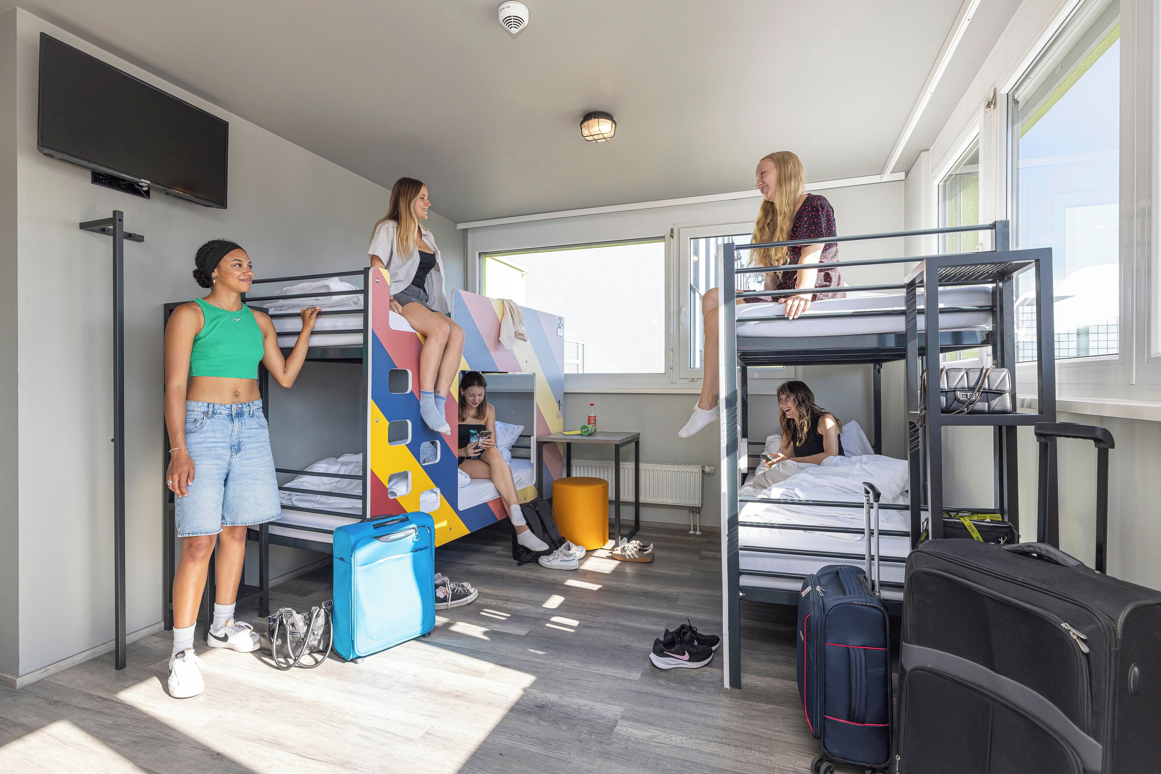 A dormitory room with bunk beds, a TV, and luggage.