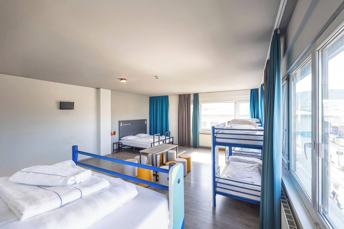 A hotel room with bunk beds, a desk, and a window with curtains.