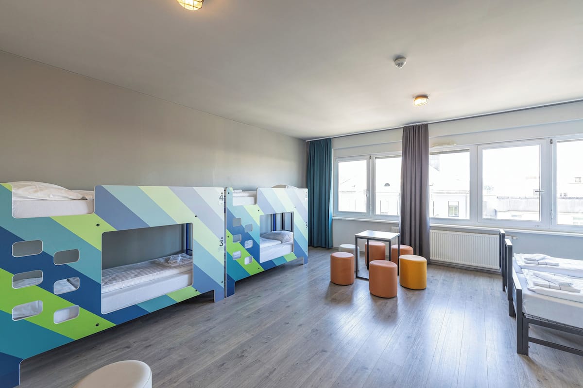 A hotel room with bunk beds, a small table, and a window with curtains.