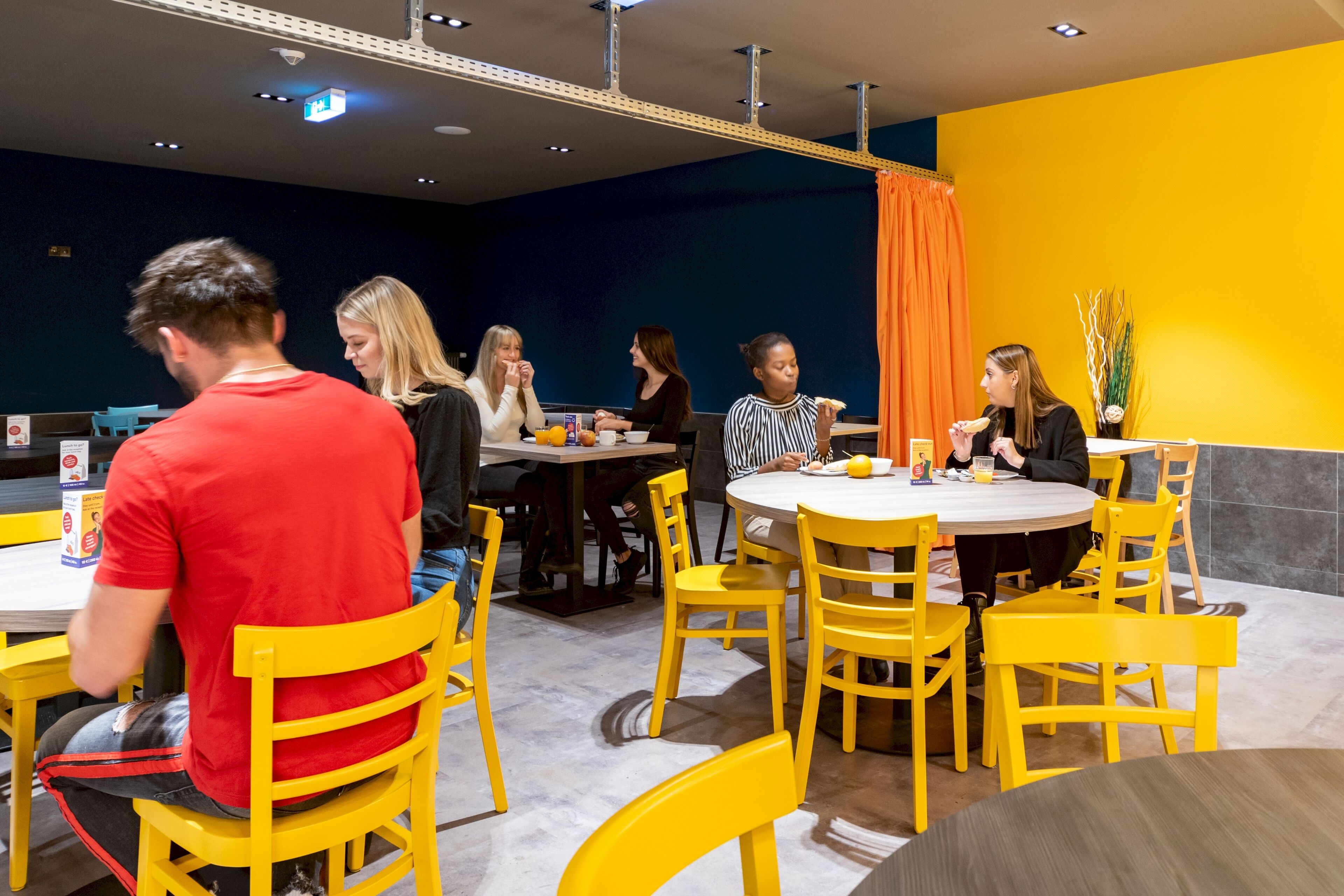 A dining area with yellow chairs and tables, a blue wall, and a yellow accent wall.