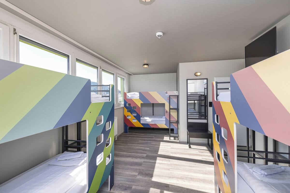 A dormitory room with bunk beds, a window, and a door.