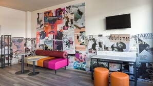 Un espacio lounge moderno con un sofá colorido, una mesita y taburetes naranjas.