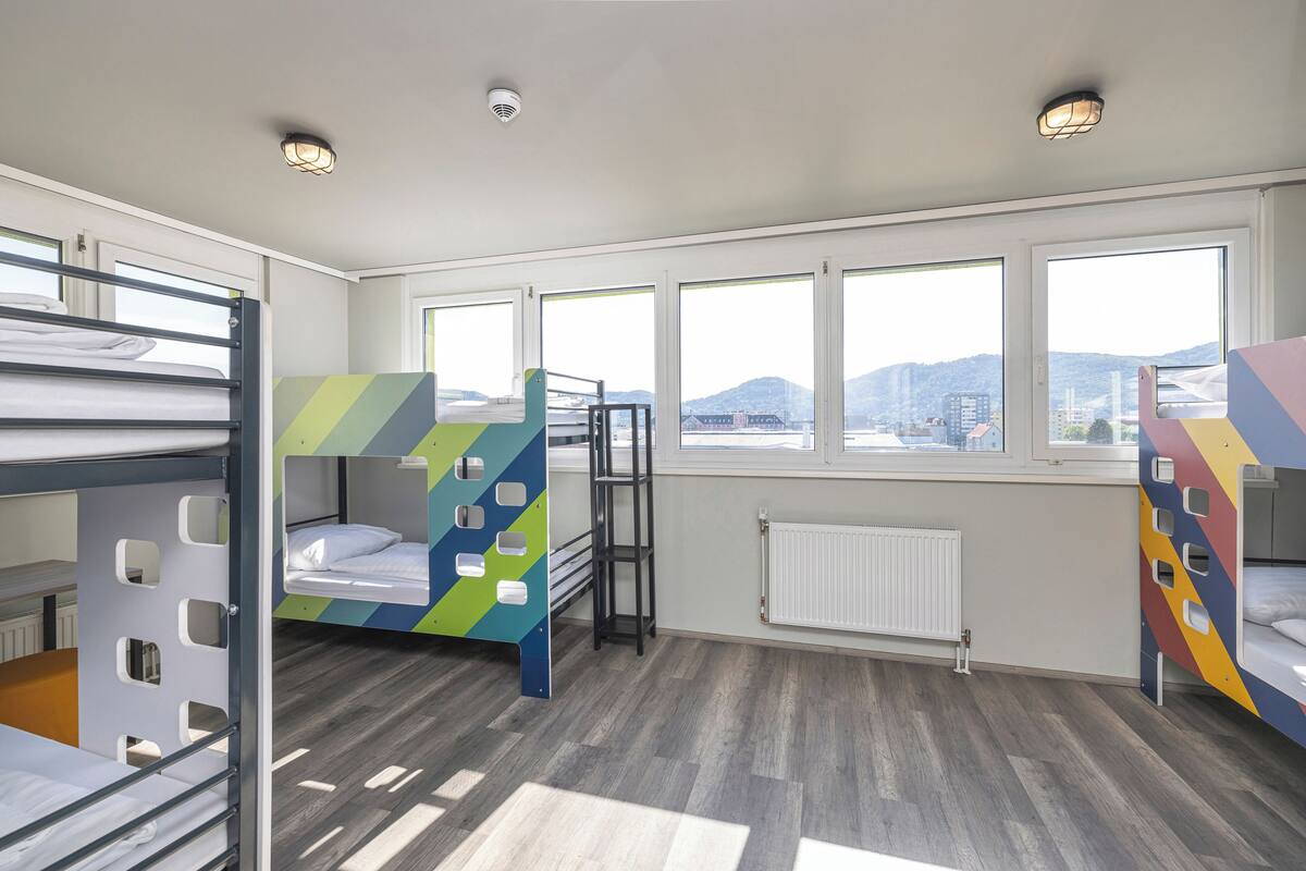 A modern hotel room with bunk beds, large windows, and a view of the city.