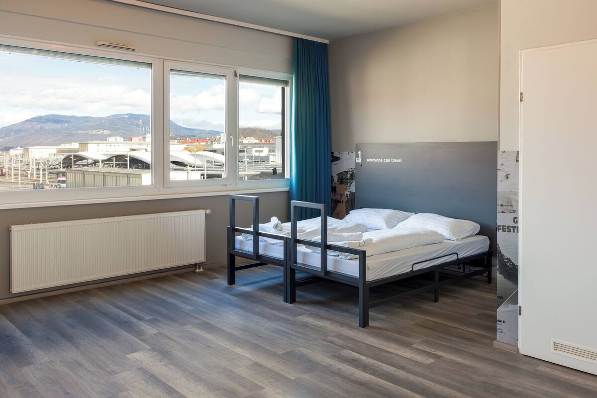 A modern hotel room with a large window, a bed, and a radiator.