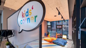 Zona infantil con un tapete de juego colorido, asientos y un gran cartel con forma de bocadillo.