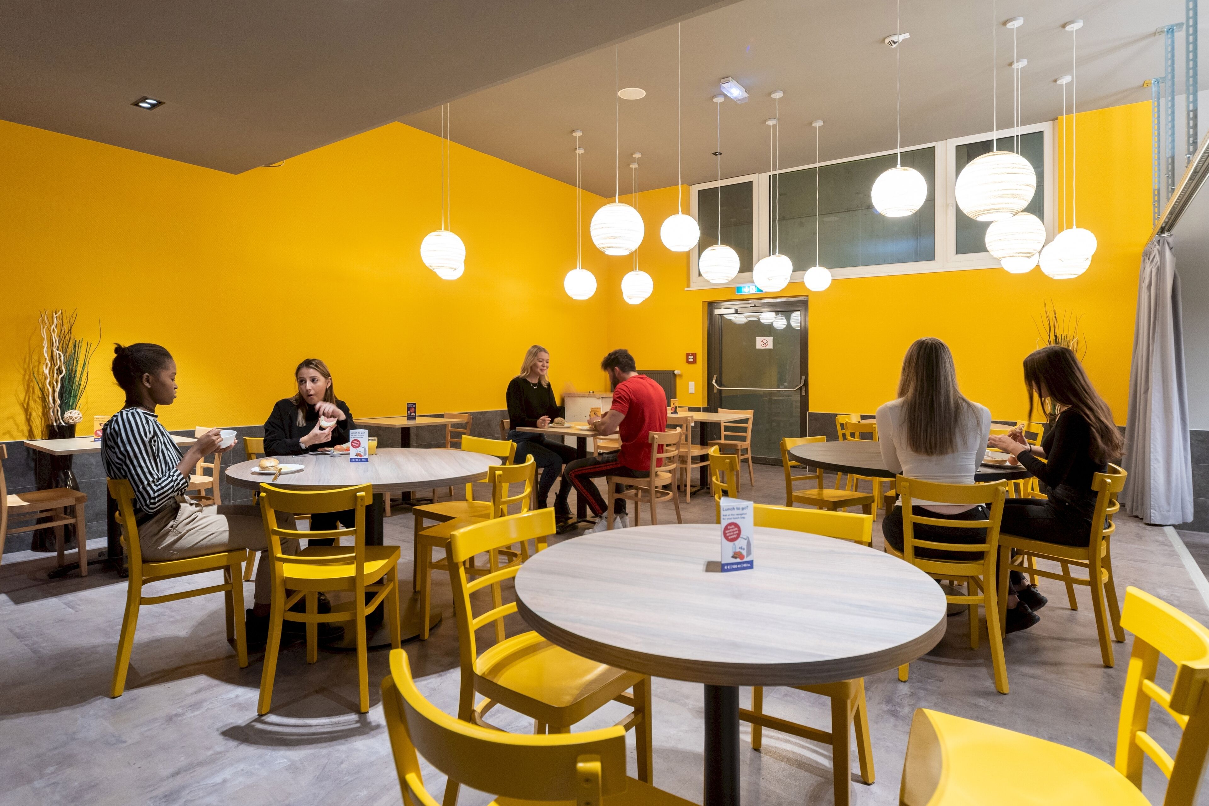 A dining area with yellow chairs and tables, a modern interior design, and pendant lighting.
