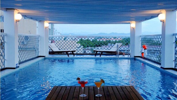 An indoor swimming pool with lounge chairs and a wooden deck, surrounded by a white fence with a view of distant mountains. - Moonlight Hotel Hue (Hue)
