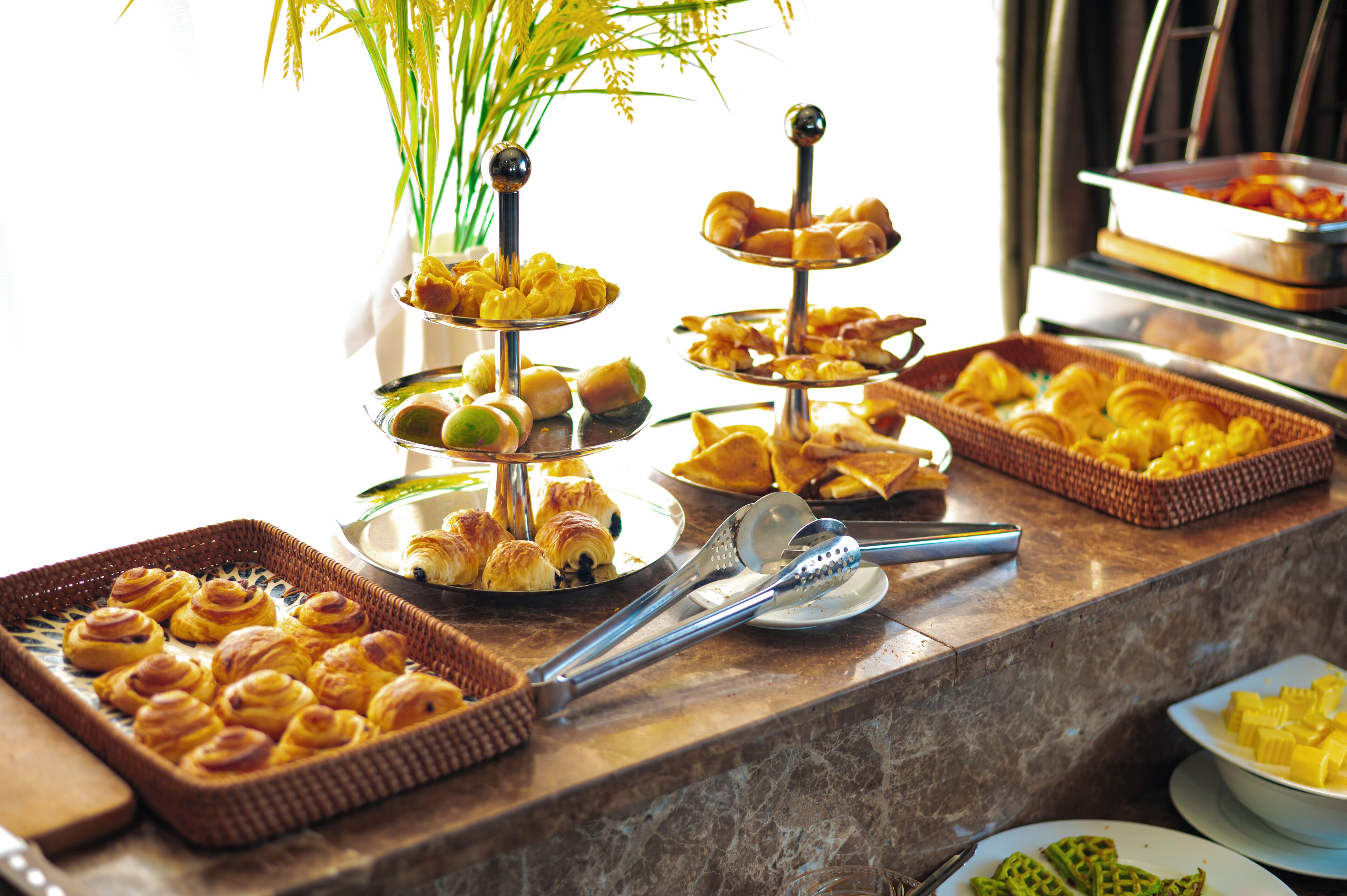 A buffet table with various pastries and desserts, including croissants and waffles, arranged on tiered stands and in baskets.