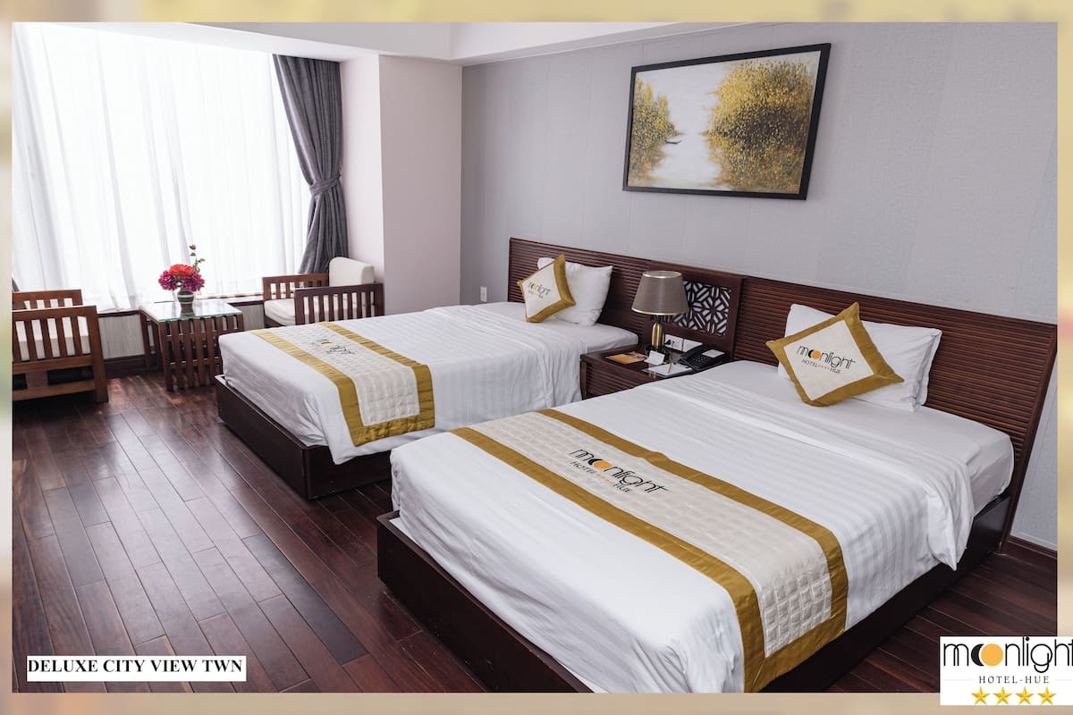 A Deluxe City View Twin room with two beds, a desk, a chair, and a window with curtains.