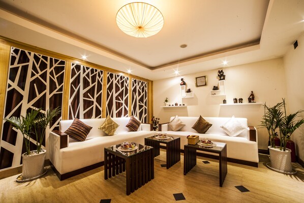 A modern living room with a white sofa, two coffee tables, decorative plants, and a geometric wall panel.