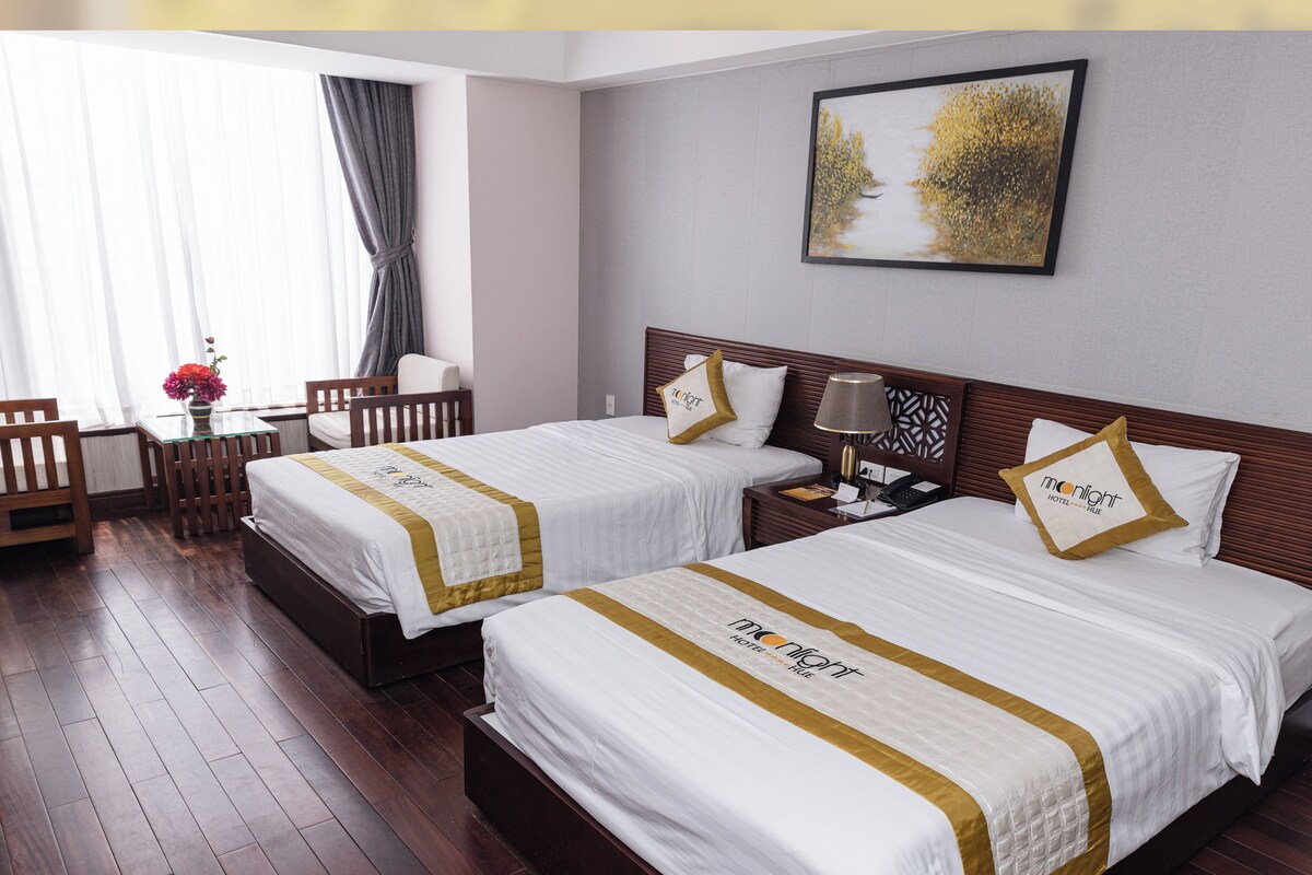 A Deluxe City View Twin room with two beds, a desk, a chair, and a window with curtains.