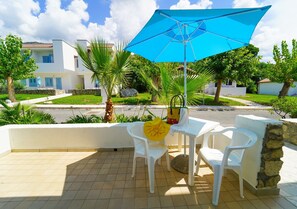 A patio with two white plastic chairs, a table, and a blue umbrella. - Villaggio Club Bahja (Paola)