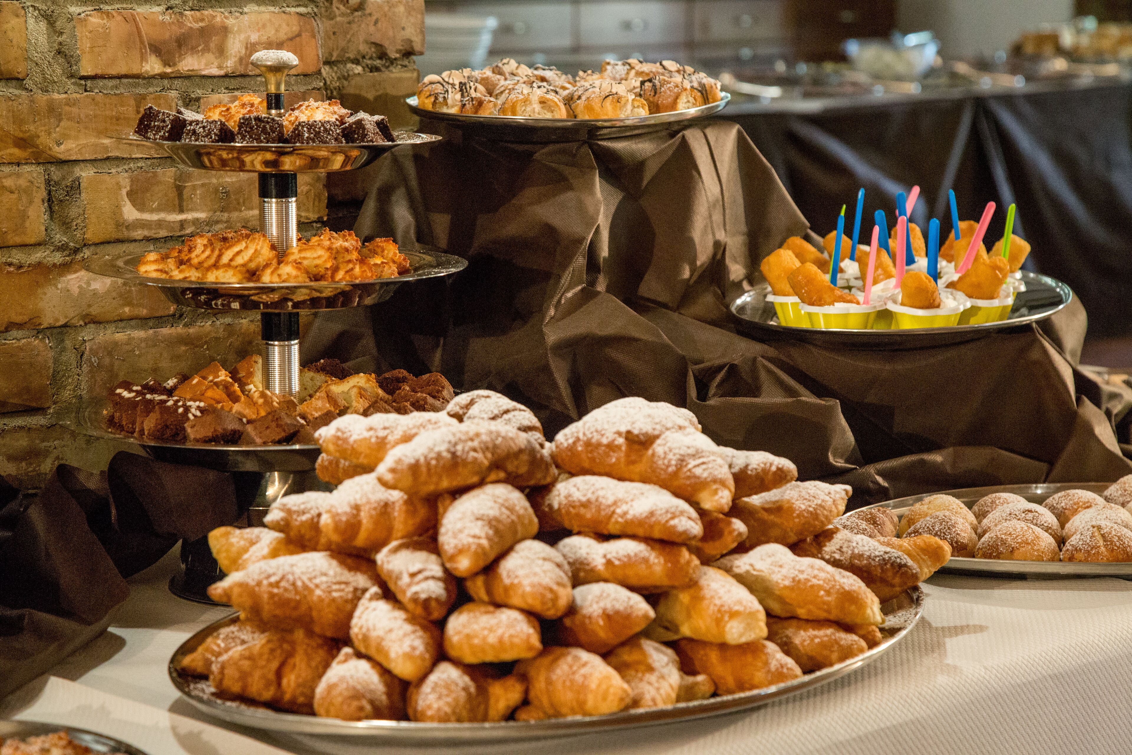 Un tavolo da buffet con diversi dolci e pasticcini, tra cui croissant e una torta con candeline.
