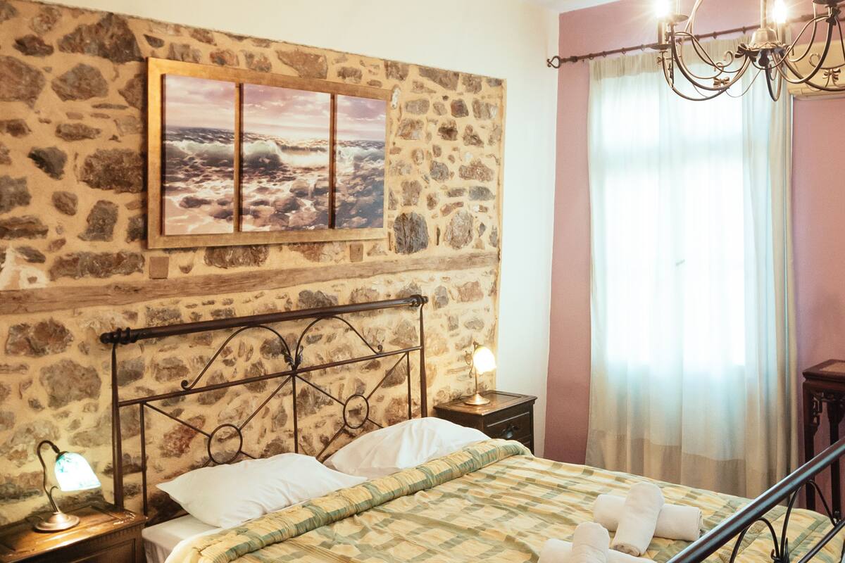 Un dormitorio con pared de piedra, cama con estructura de metal, suelo de madera, mesita de noche con lámpara y candelabro.