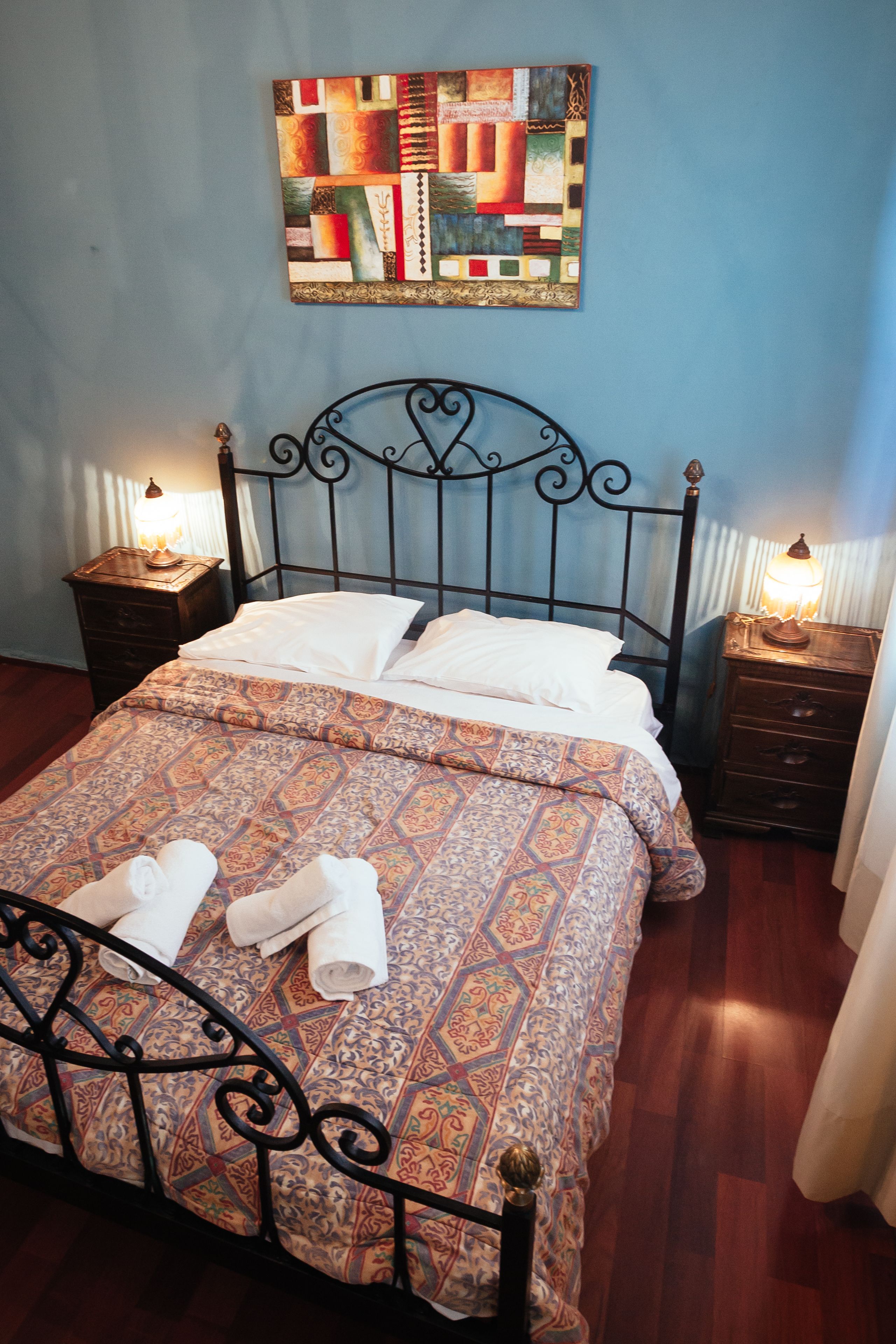 A neatly made bed with patterned bedding, a headboard, and two bedside tables with lamps.