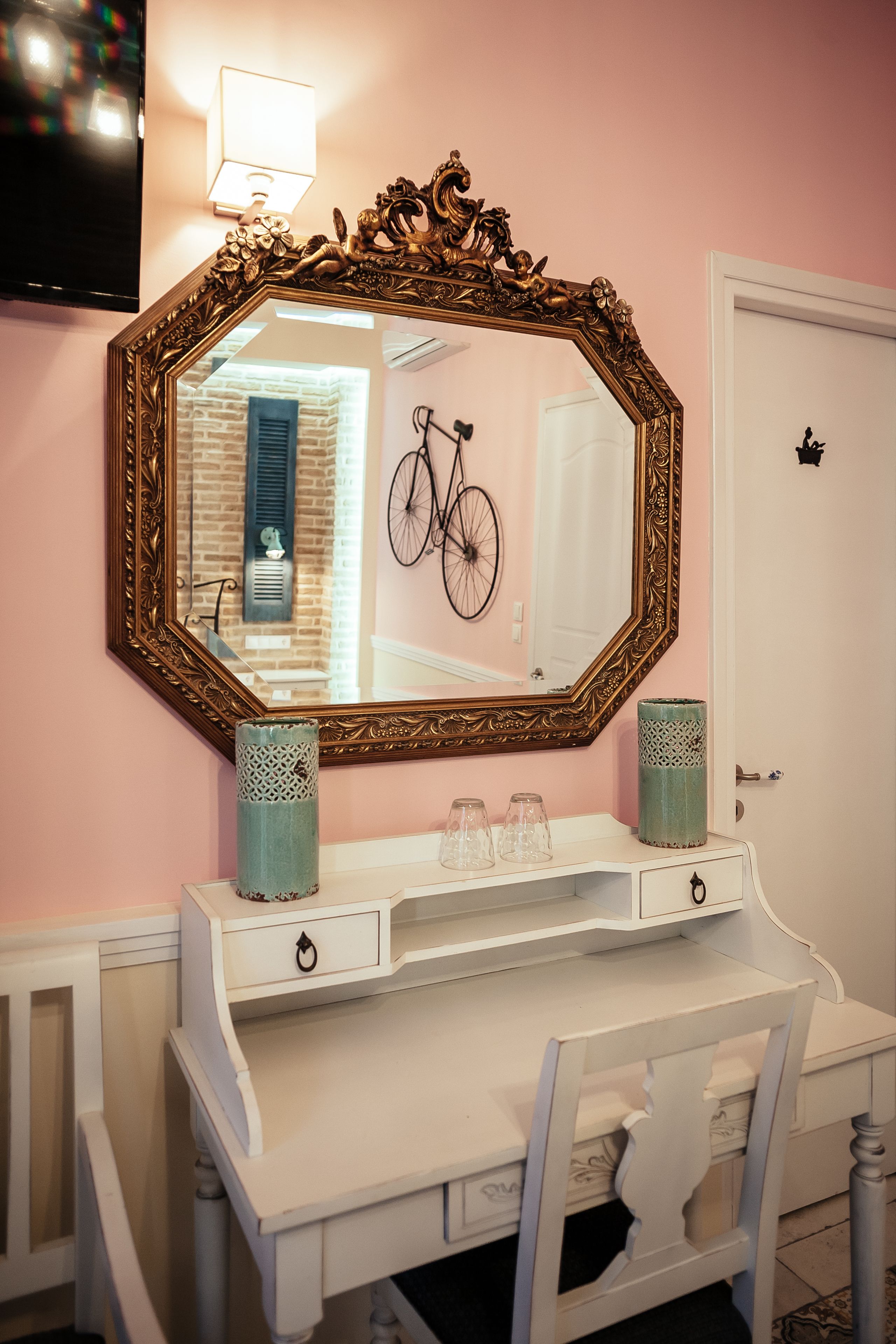 A white vanity with a large ornate mirror, two decorative vases, and a bicycle in the reflection.