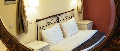 A bedroom with a bed, bedside tables, a nightstand, a mirror, and framed pictures on the wall.
