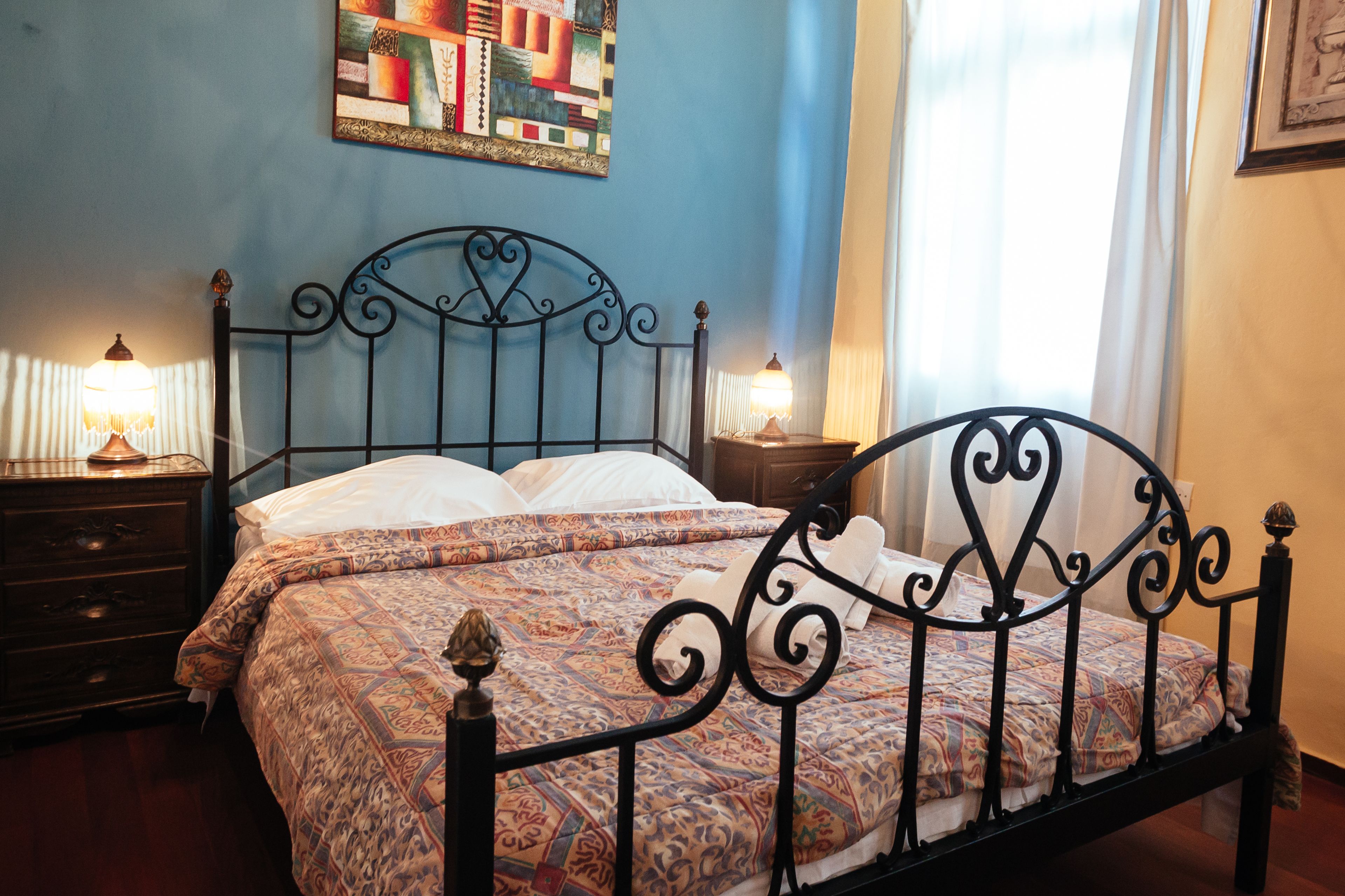 A neatly made bed with a patterned bedspread and pillows, a dark metal headboard, and bedside lamps.