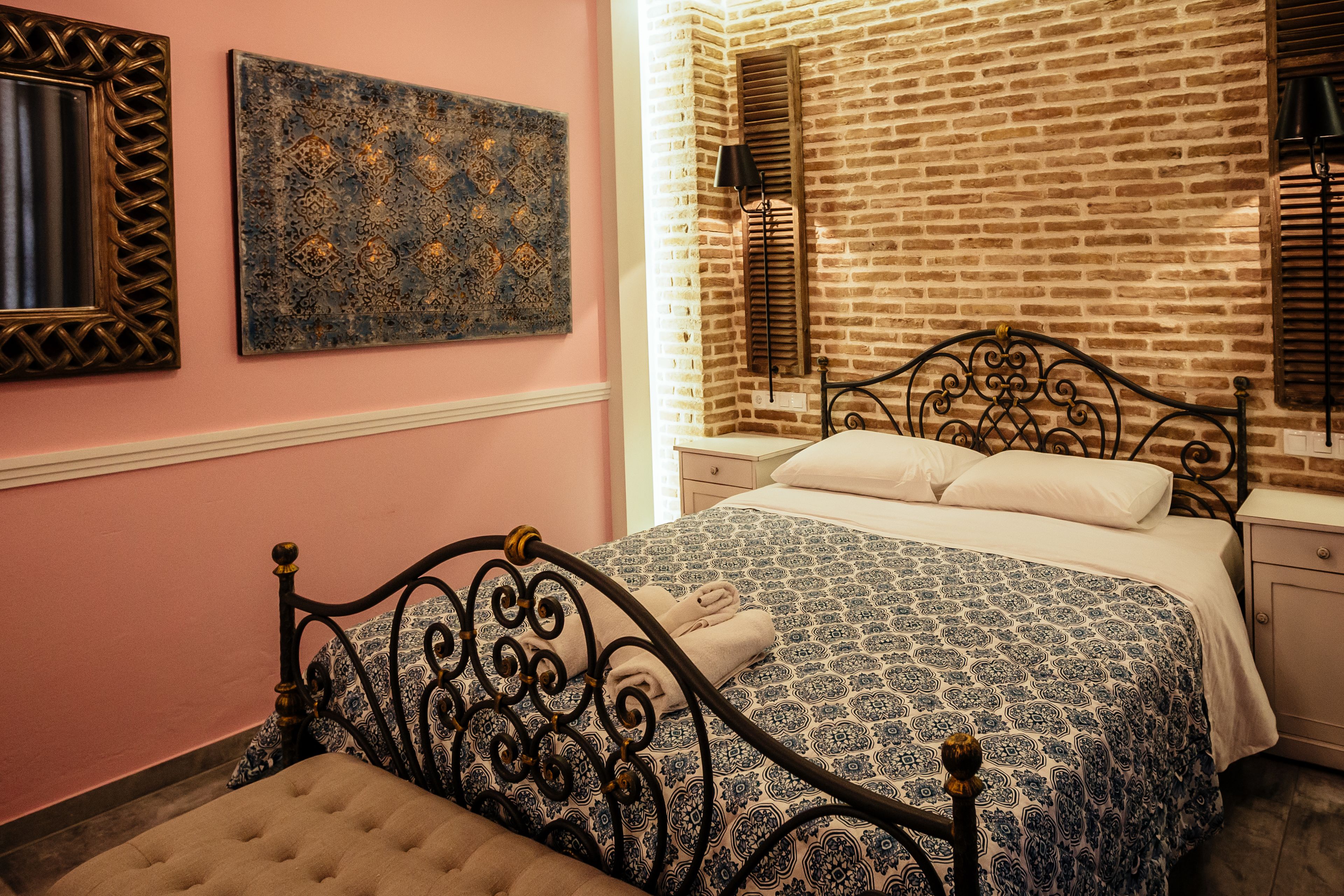 Un dormitorio con pared de ladrillo, una cama con colcha estampada, una mesita de noche y una lámpara de pared.
