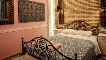 Un dormitorio con pared de ladrillo, una cama con colcha estampada, una mesita de noche y una lámpara de pared.