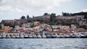 Un pueblo costero con edificios históricos, una colina fortificada y un puerto deportivo con barcos.