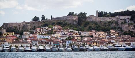 A coastal town with historic buildings, a fortified hill, and a marina with boats.