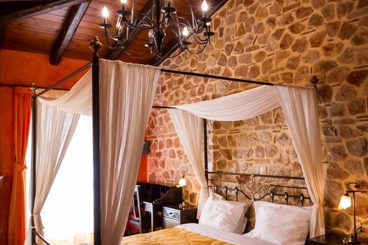 Una cama con dosel y colcha amarilla, una pared de piedra y una araña.