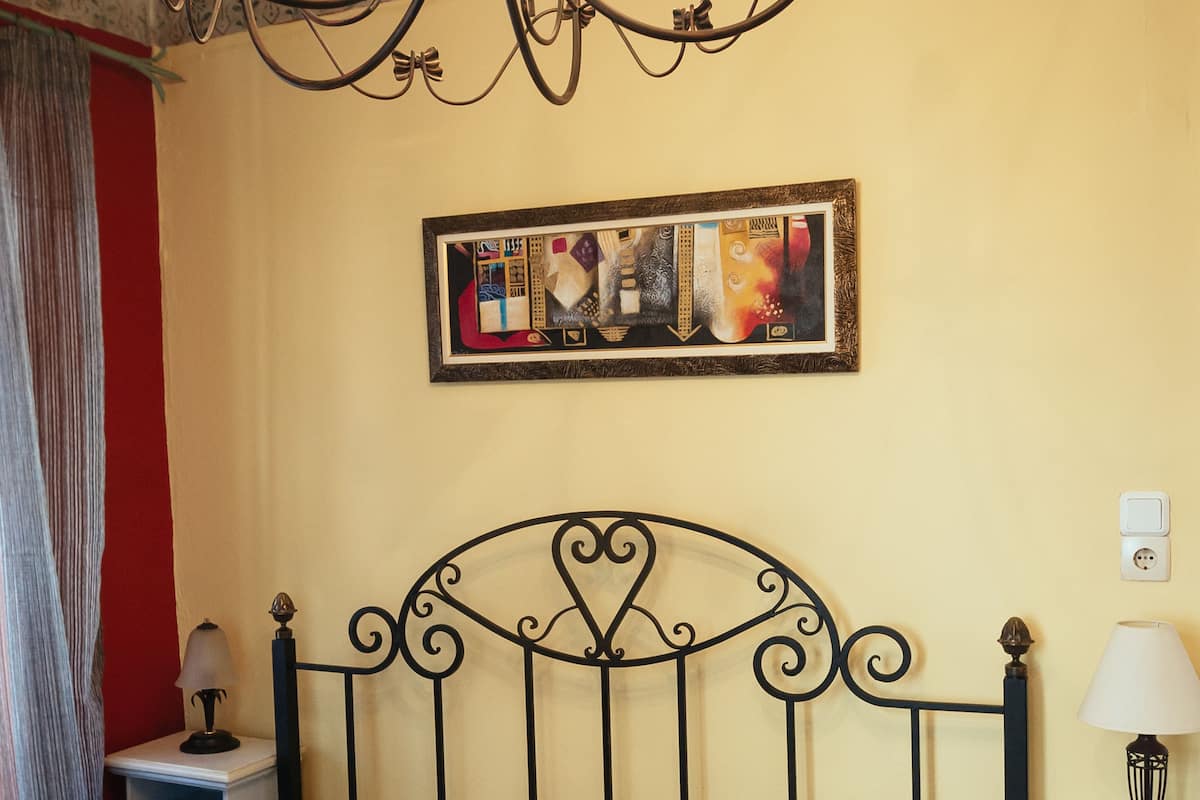 Una cama con una colcha estampada, un cabecero de metal negro, un cuadro colgado en la pared y una mesita de noche con una lámpara.