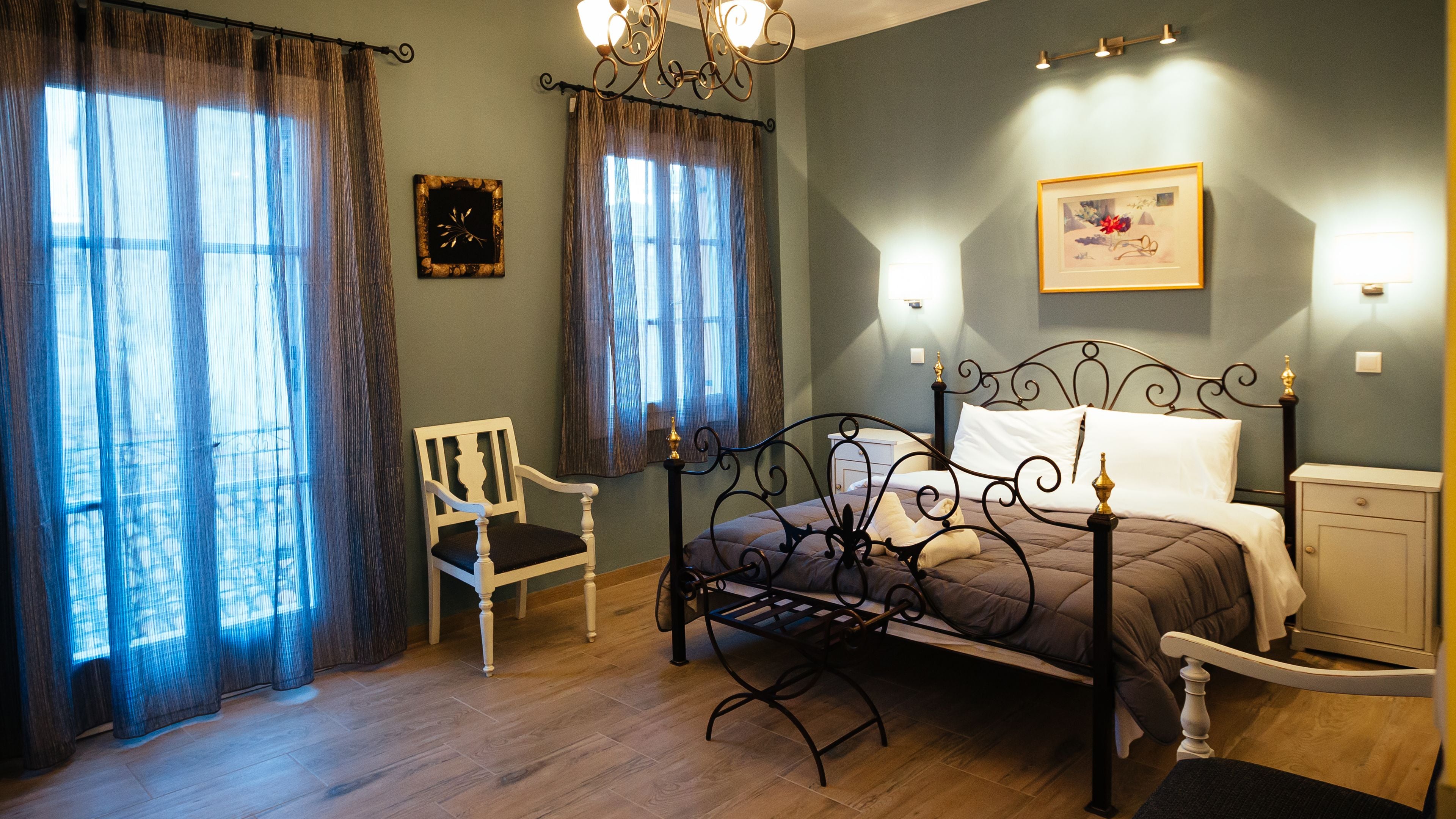 A bedroom with a bed, a chair, a bedside table, a nightstand, a lamp, a window with curtains, and a wall clock.