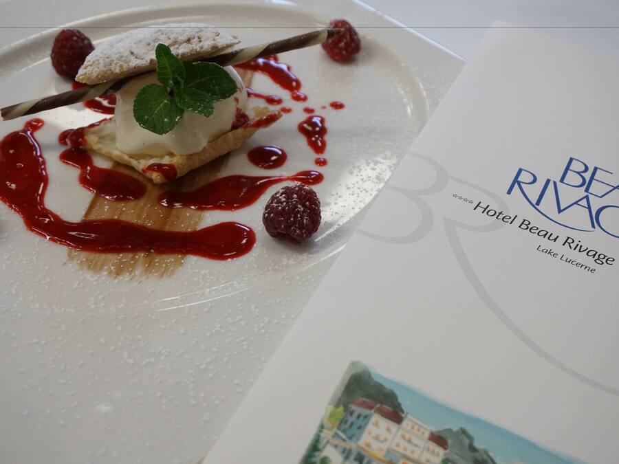 A dessert plate with a scoop of ice cream, raspberries, and a mint leaf on a white plate.