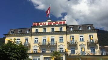 A hotel with a prominent "BEAU RIVAGE" sign, multiple balconies with yellow umbrellas, and a flag on top.