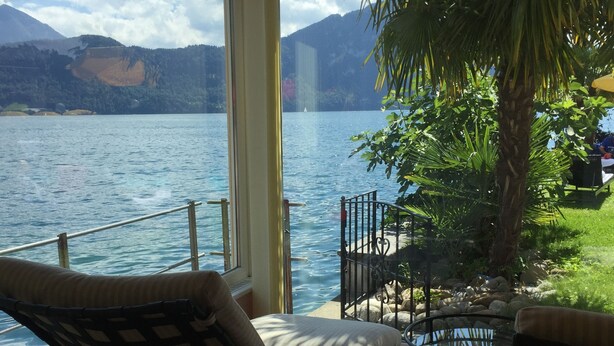 Een balkon met uitzicht op een meer, een palmboom en tuinmeubilair.