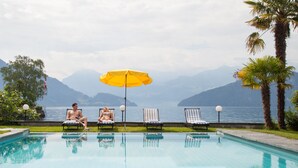 Zwembad met ligbedden en parasol, met uitzicht op een waterlichaam en bergen.