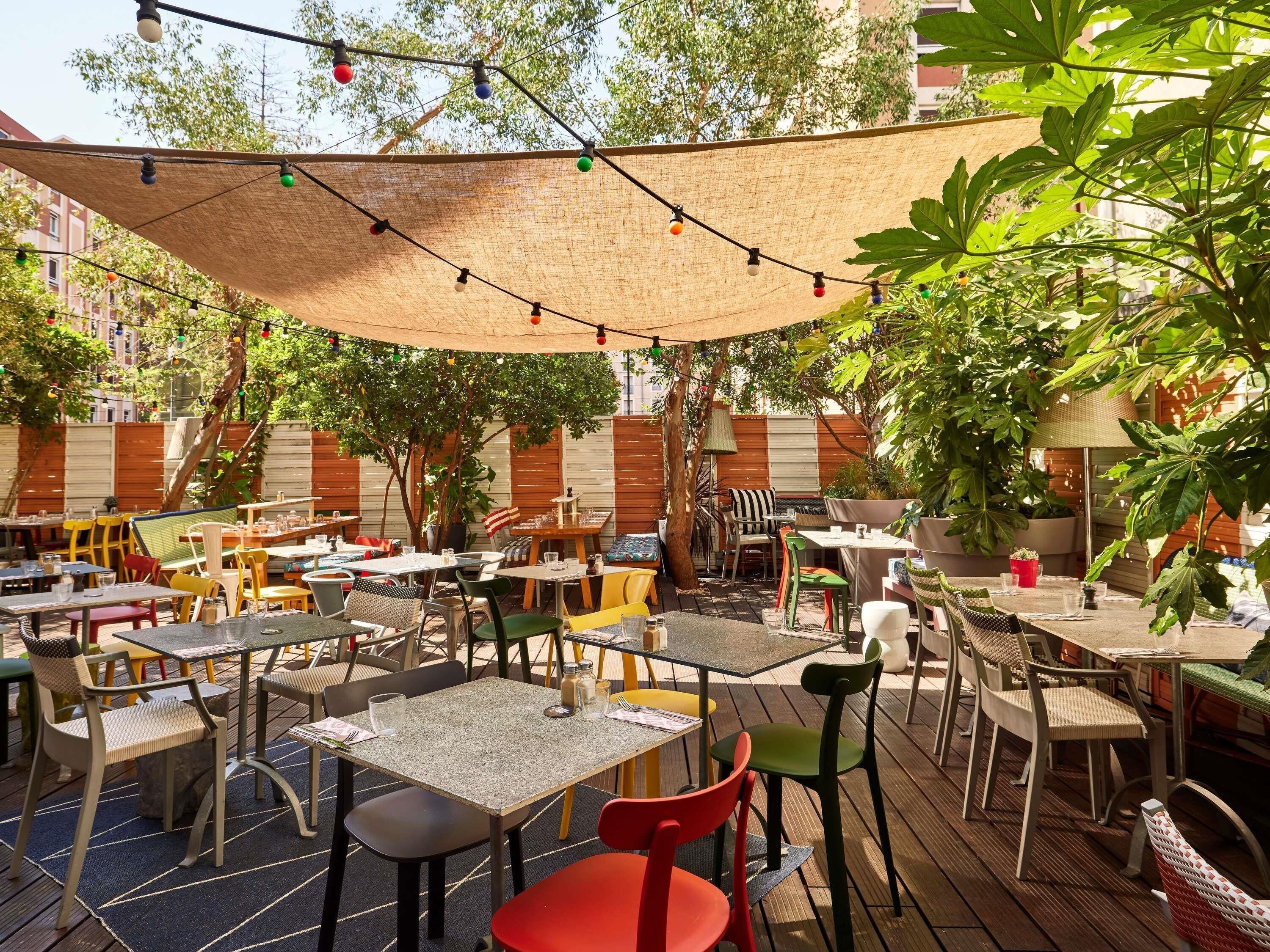 Un espace extérieur aménagé en terrasse, avec des tables et des chaises, des guirlandes lumineuses et un auvent ombragé.