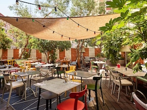 Un espace extérieur aménagé en terrasse, avec des tables et des chaises, des guirlandes lumineuses et un auvent ombragé.