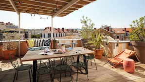 A rooftop terrace with a wooden table, chairs, a sofa, and potted plants. - Mama Shelter Lyon (Lyon)