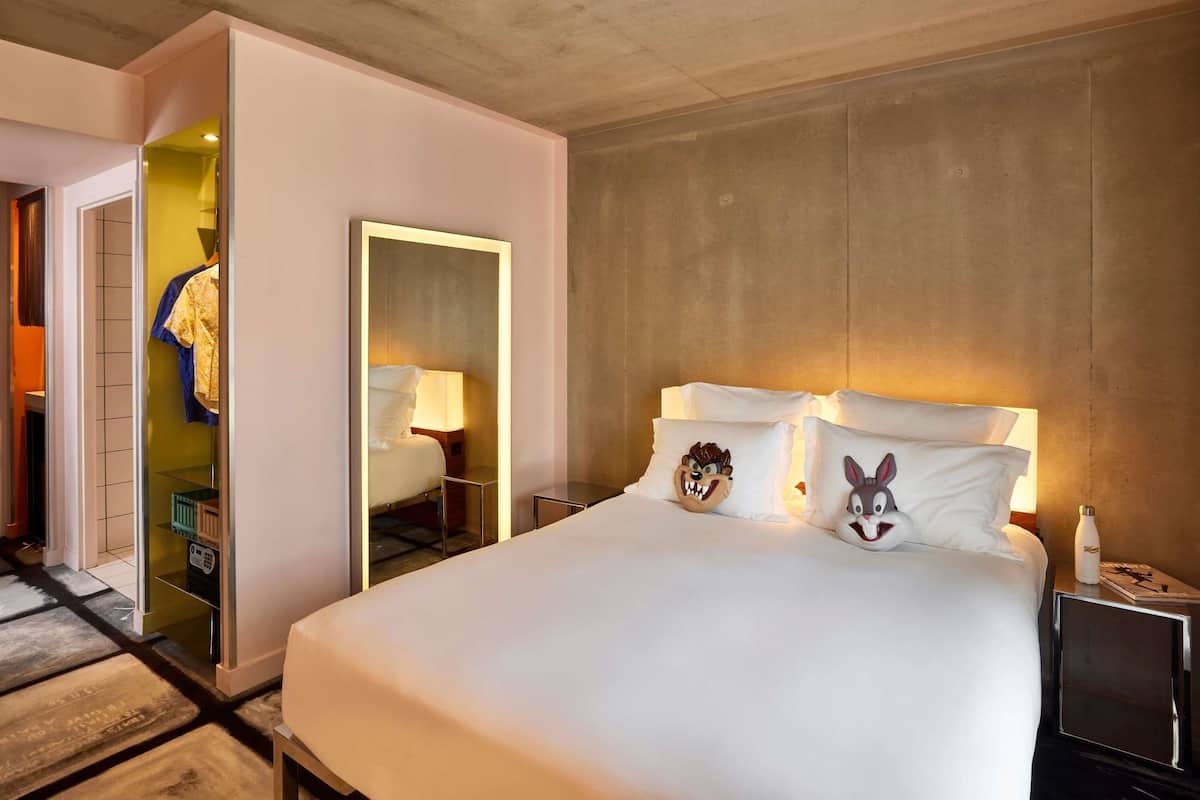 Une chambre d’hôtel avec un grand lit, une table de chevet avec une lampe, un miroir et une armoire avec un miroir.