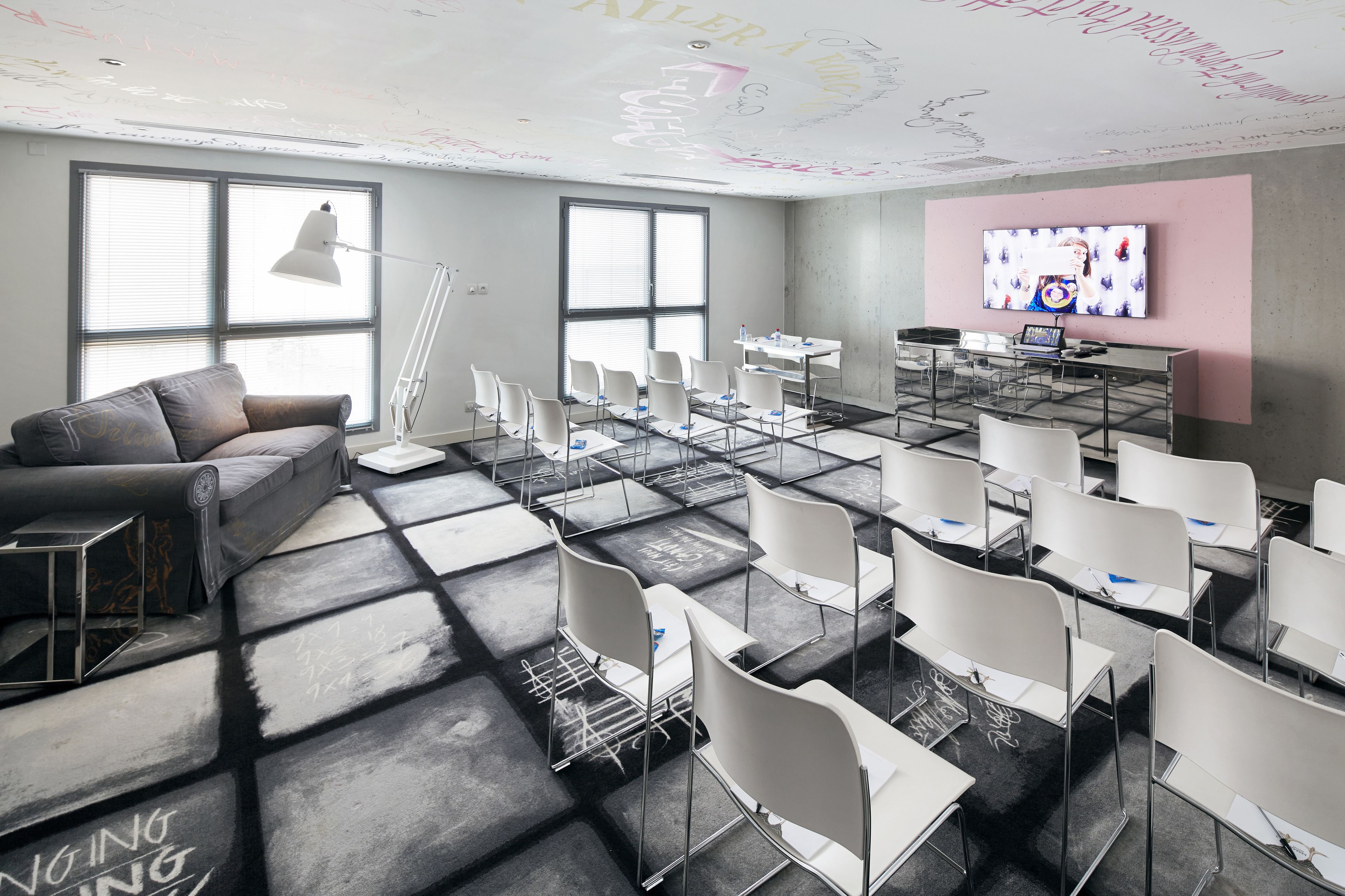 A modern conference room with white chairs, a grey sofa, and a large TV screen on the wall.