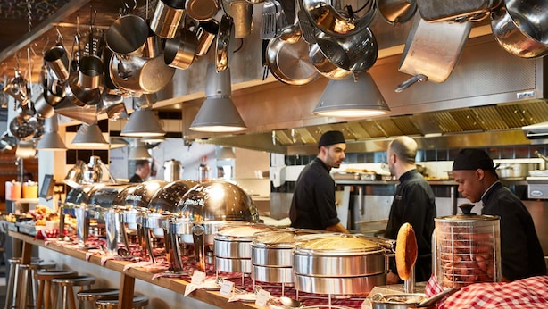 A buffet setup with multiple food containers, a counter with stools, and overhead hanging pots. - Mama Shelter Lyon (Lyon)