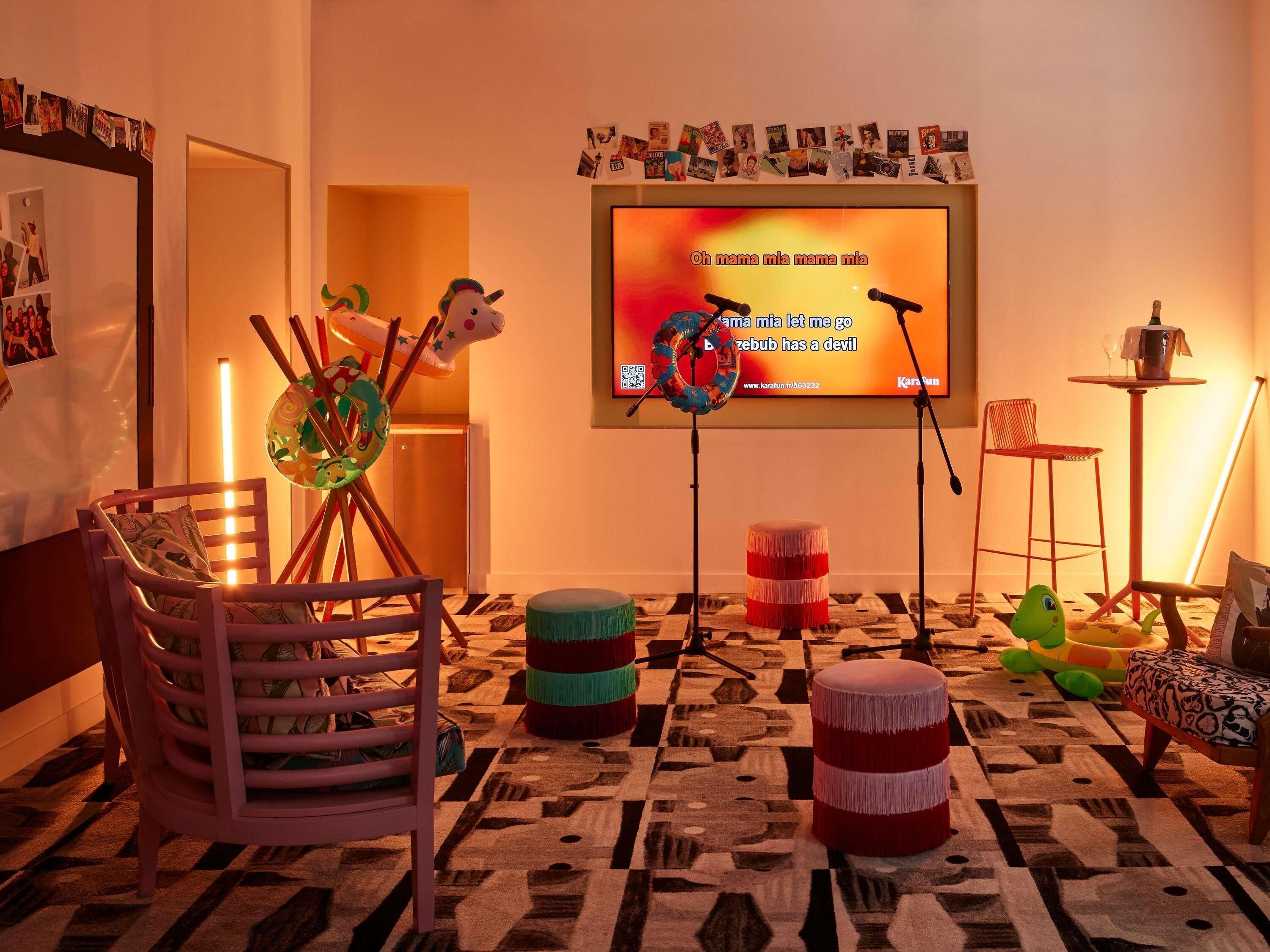 Une pièce chaleureuse avec un téléviseur diffusant une chanson, un fauteuil coloré, des poufs et un tapis à motifs.