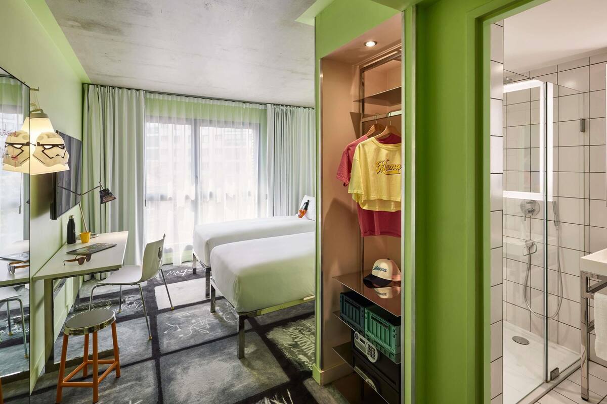 Une chambre d’hôtel équipée d’un lit, d’un bureau, d’une chaise et d’un dressing avec des vêtements suspendus.