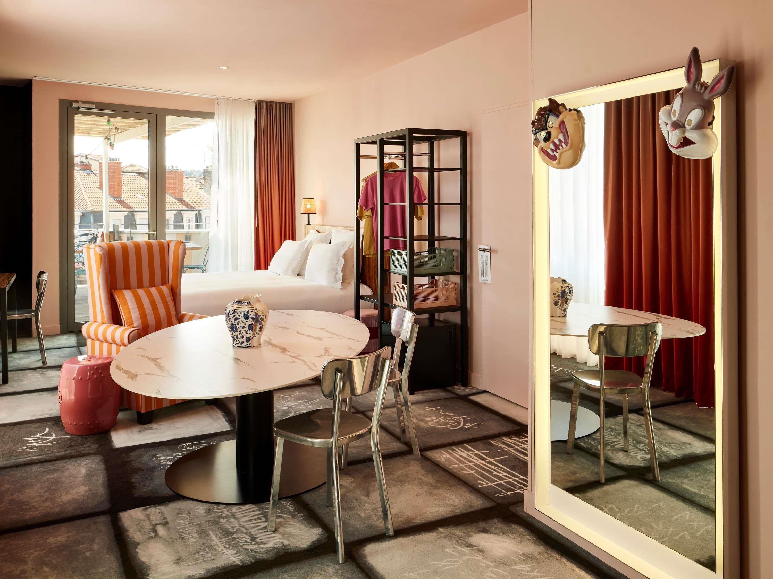 Une chambre d’hôtel comprenant un lit, une table à manger avec des chaises, un grand miroir et une armoire.