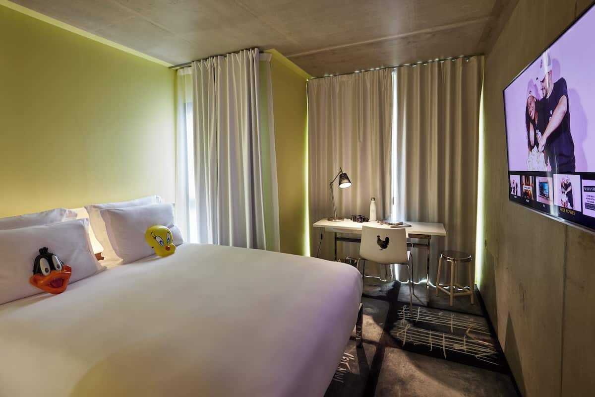 Une chambre d’hôtel avec un lit, un bureau, une chaise, une télévision et des rideaux.