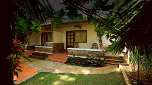 A house with a stone exterior, a small porch with a bench, and a garden area with a pathway. - Glenmore Resorts (Devikolam)