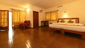 A bedroom with a wooden bed, a desk, and a chair. There is a door and a window with curtains. - Glenmore Resorts (Devikolam)